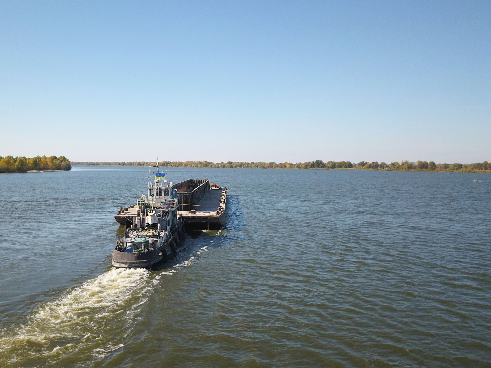 A tugboat ship pushes a barge upstream of the river to transport bulk materials. Aerial photography with a quadcopter or a drone. Panorama of the Dnieper - the main water transport artery of Ukraine